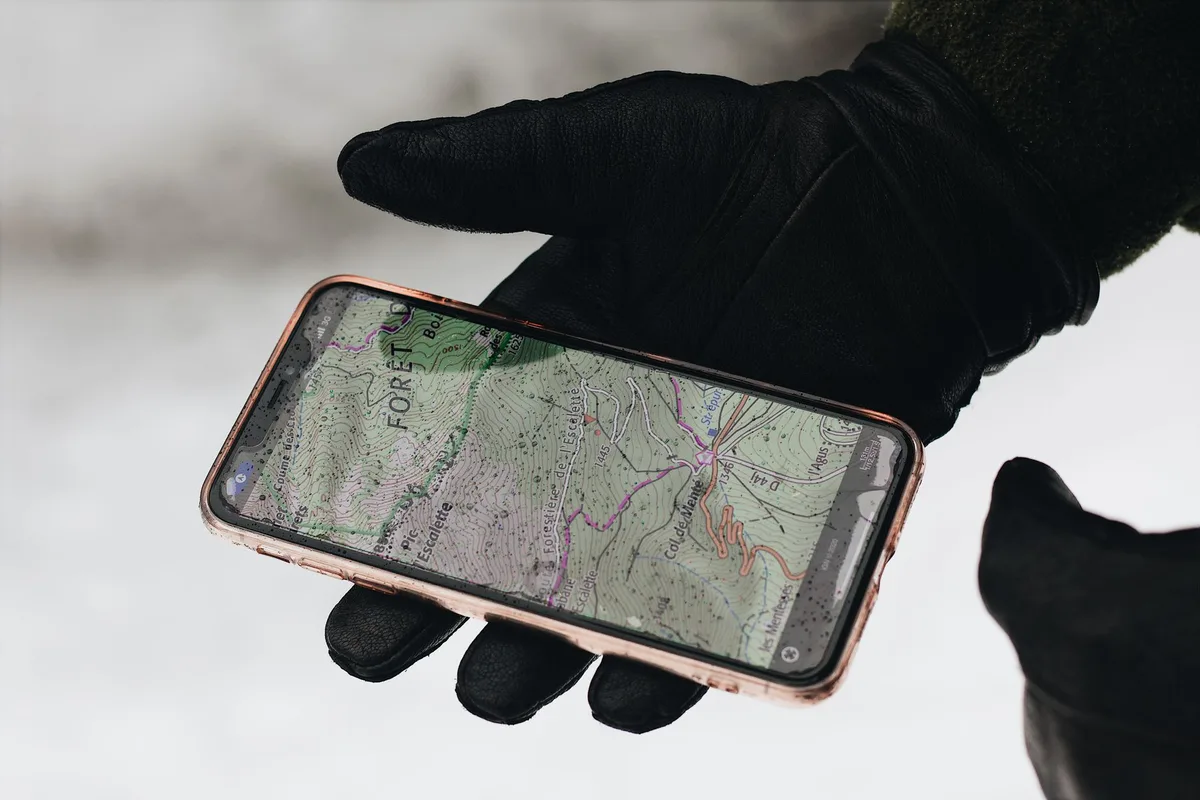 Randonneur consultant une carte numérique sur son téléphone lors d'une sortie en forêt.