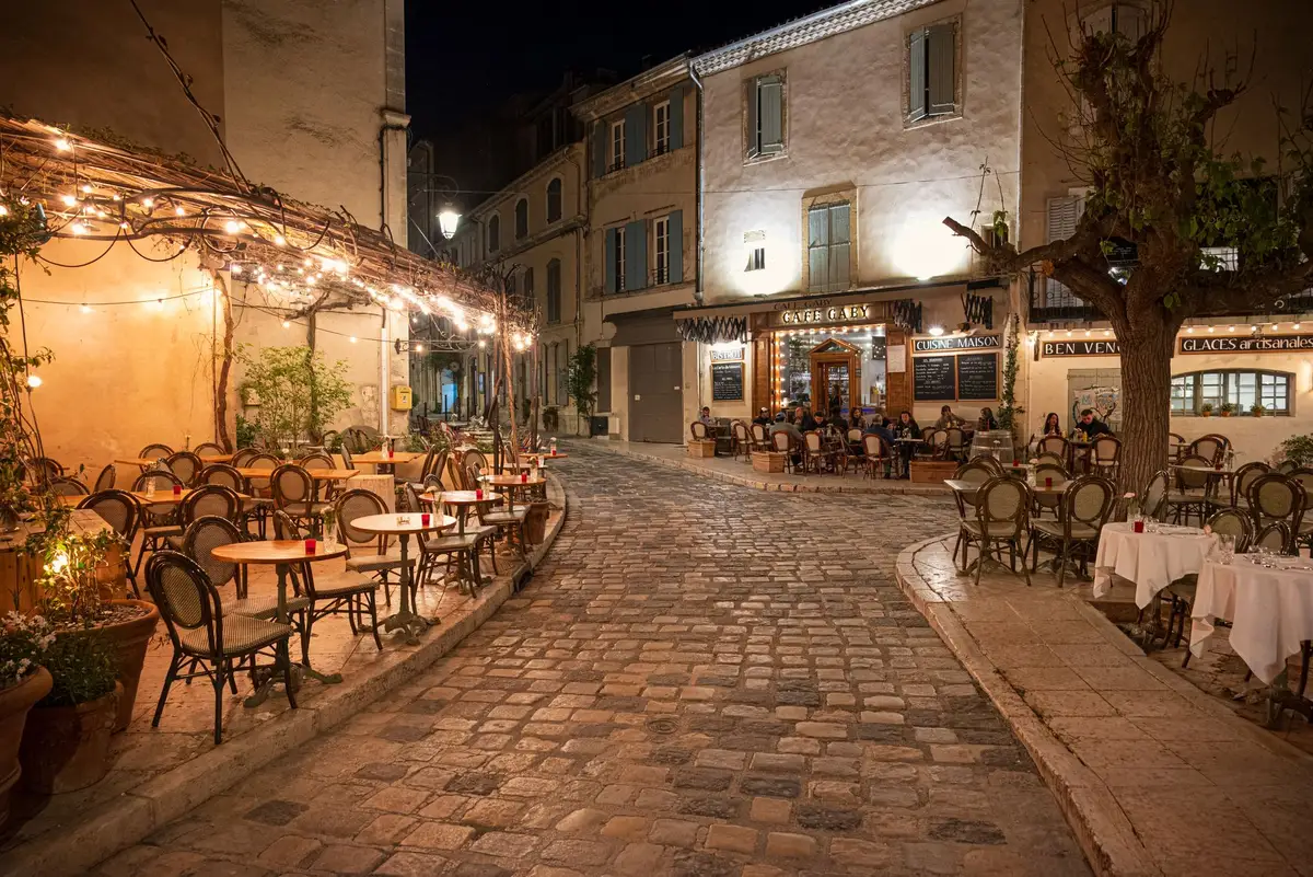 Terrasse ombragée avec tables et chaises dans une place provençale, ambiance conviviale
