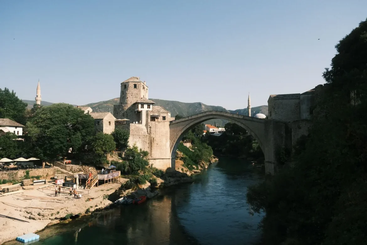 Pont ancien enjambant un fleuve avec remparts et tours médiévales en arrière-plan sous lumière dorée