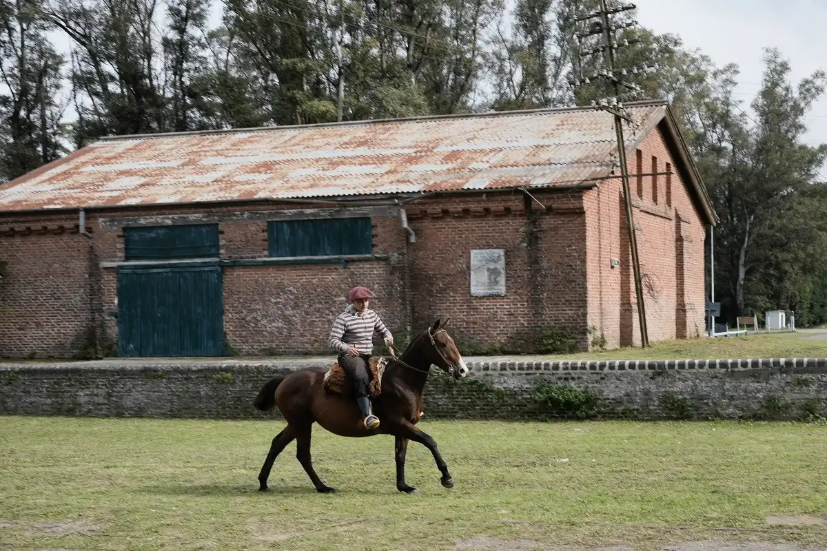Cavalier galopant dans les pampas près d'une estancia traditionnelle