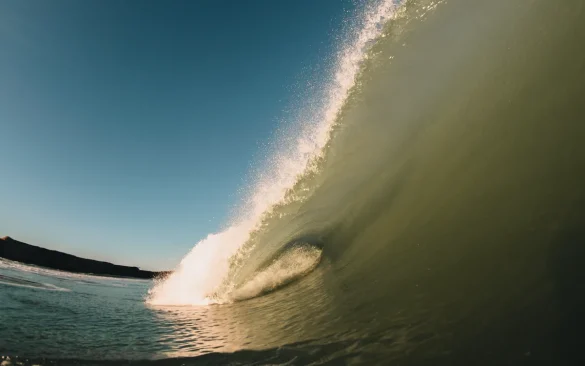 Surfer chevauchant un tube parfait sur un reef break avec falaises volcaniques en arrière-plan