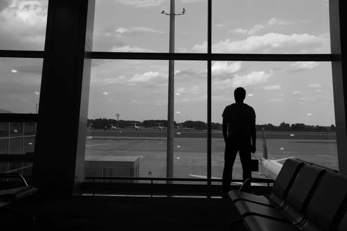 Passager à la fenêtre d'un salon d'aéroport, contemplant les pistes d'envol